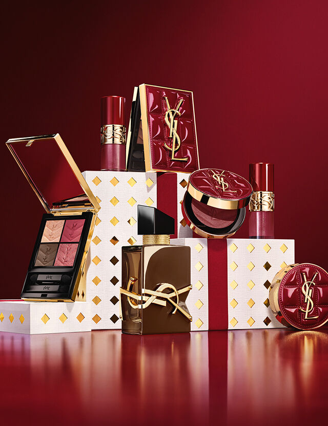 La collezione trucco e il set fragranza YSL Holiday 2026 su piedistalli bianchi punteggiati d’oro in un tripudio di bordeaux.