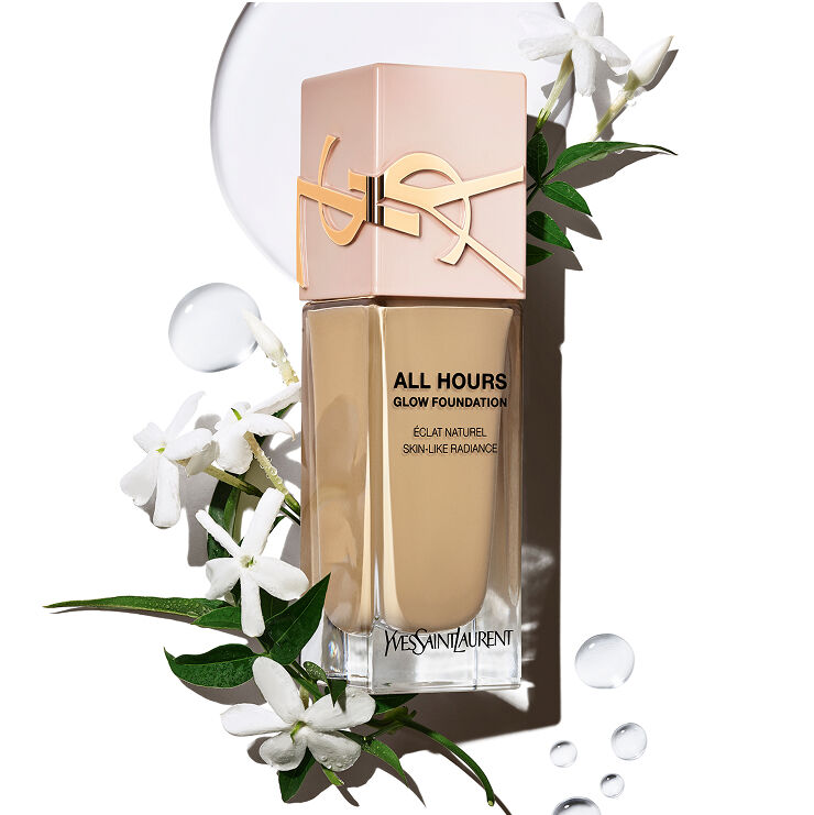 Flacone del fondotinta YSL All Hours Glow con 'Éclat Naturel Skin-Like Radiance' circondato da fiori di gelsomino bianchi e goccioline d'acqua limpida, a suggerire ingredienti naturali e idratazione.