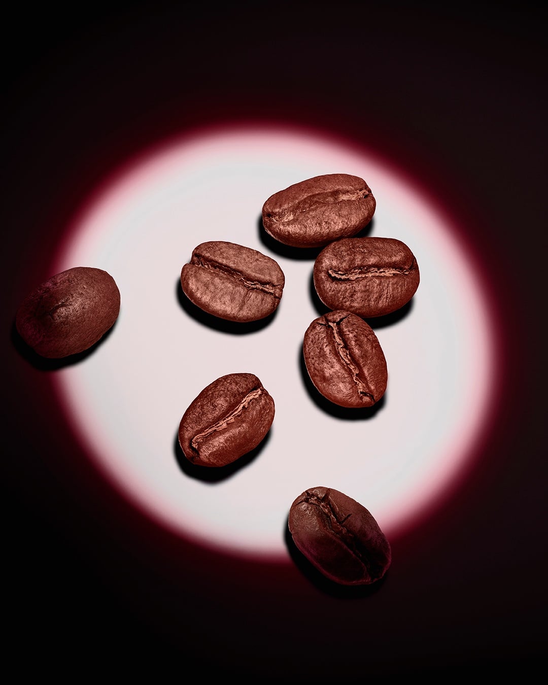 Un gruppo di chicchi di caffè tostati, illuminati da un fascio circolare rosa su fondo scuro.