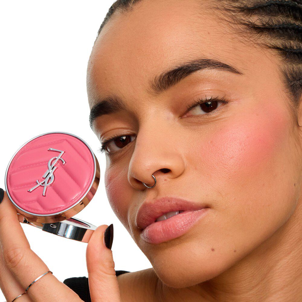 Primo piano di una modella che stringe lo YSL Make Me Blush Lifted Glow Cream Blush, con un bagliore radioso e sollevato sulle sue zigomi. Meglio. 