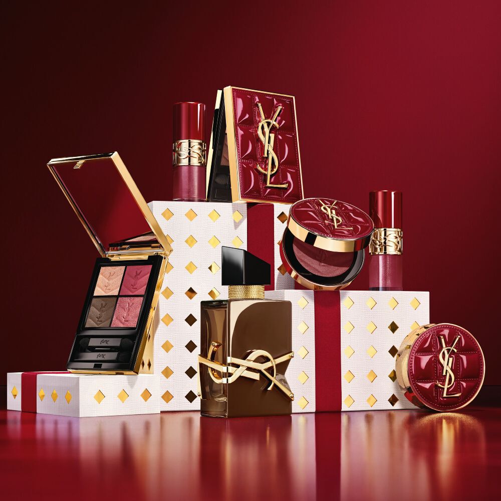 La collezione trucco e il set fragranza YSL Holiday 2026 su piedistalli bianchi punteggiati d’oro in un tripudio di bordeaux.