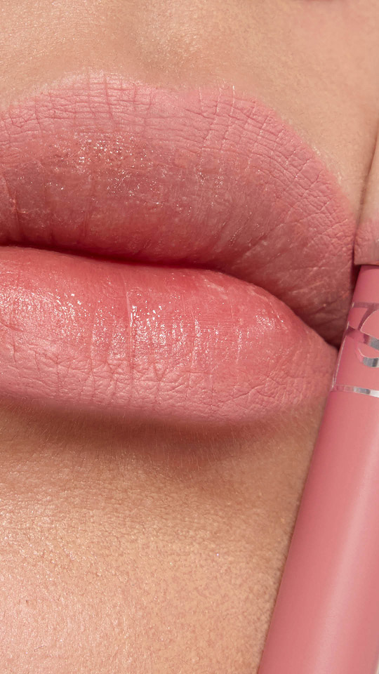 Primo piano verticale di labbra con rossetto opaco rosa tenue e relativo tubetto.