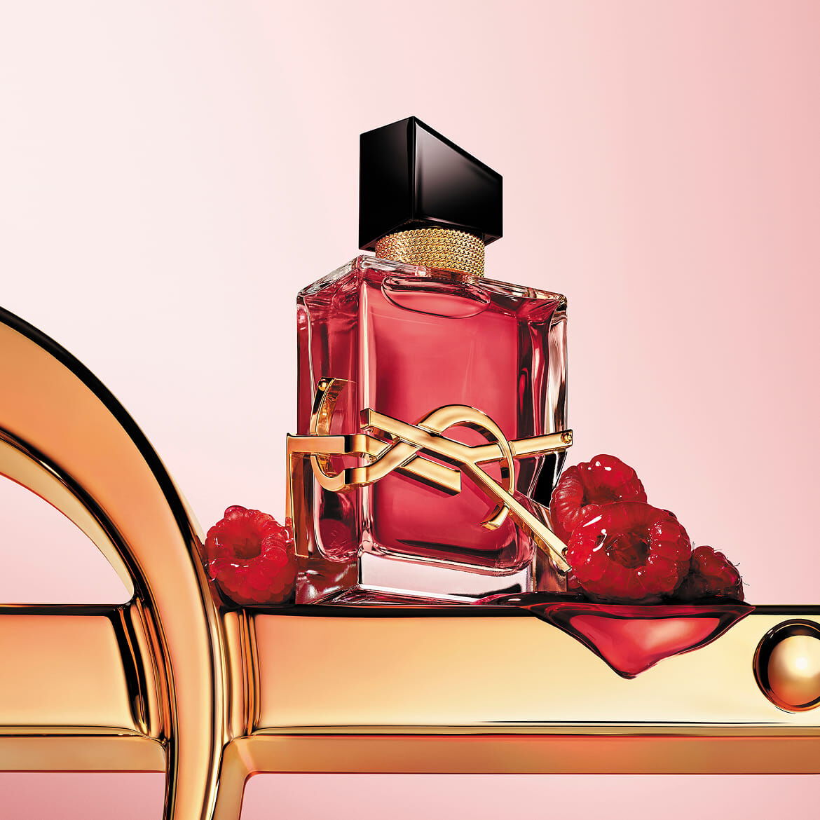 Primo piano di flacone di profumo YSL rosso con logo dorato su una superficie dorata con lamponi.