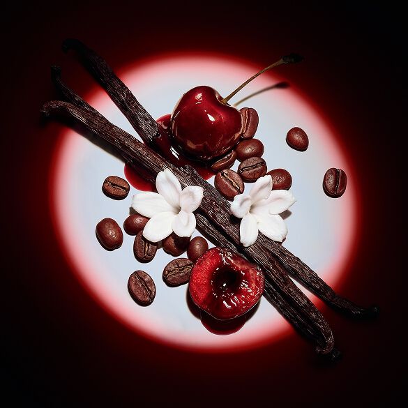 Primo piano di succose ciliegie rosse, fiori di gelsomino, baccelli di vaniglia e chicchi di caffè, illuminati da un fascio di luce teatrale per Black Opium Eau de Parfum Over Red.