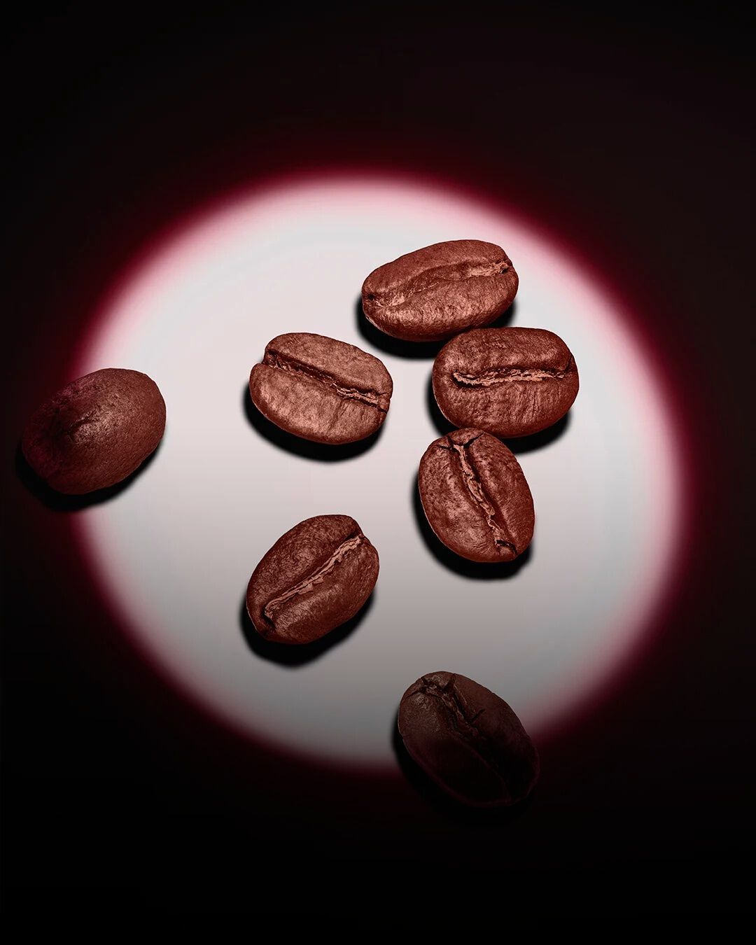 Un gruppo di chicchi di caffè tostati, illuminati da un cerchio di luce rosa su fondo scuro.