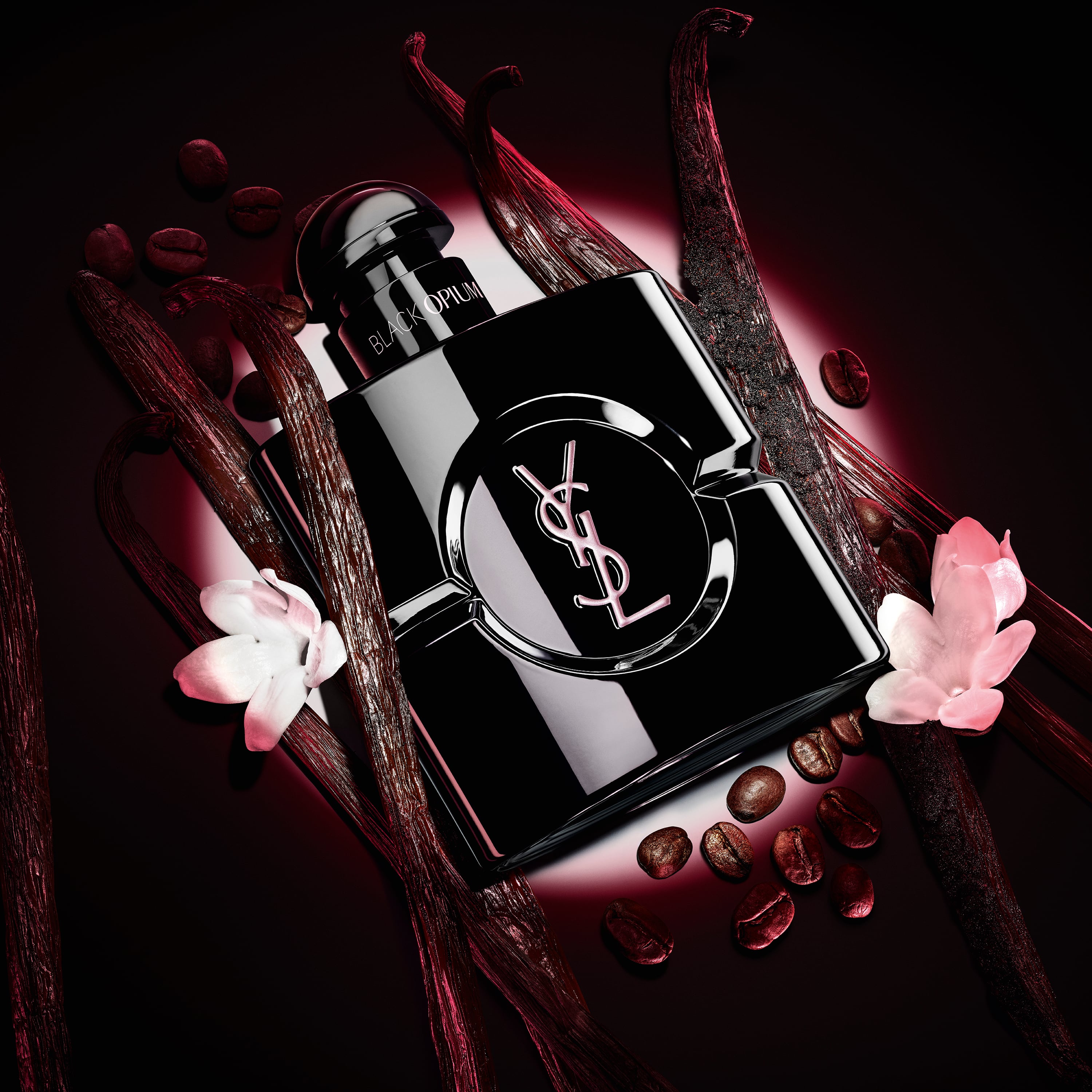 Il flacone Black Opium Le Parfum in nero lucido, circondato da scure bacche di vaniglia e gelsomino bianco.