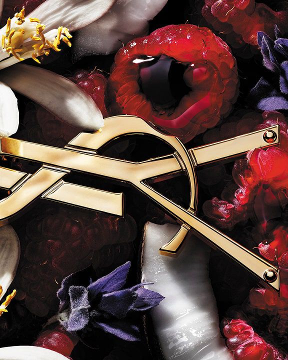 Logo YSL circondato da lamponi, fiori bianchi e viola e cocco.
