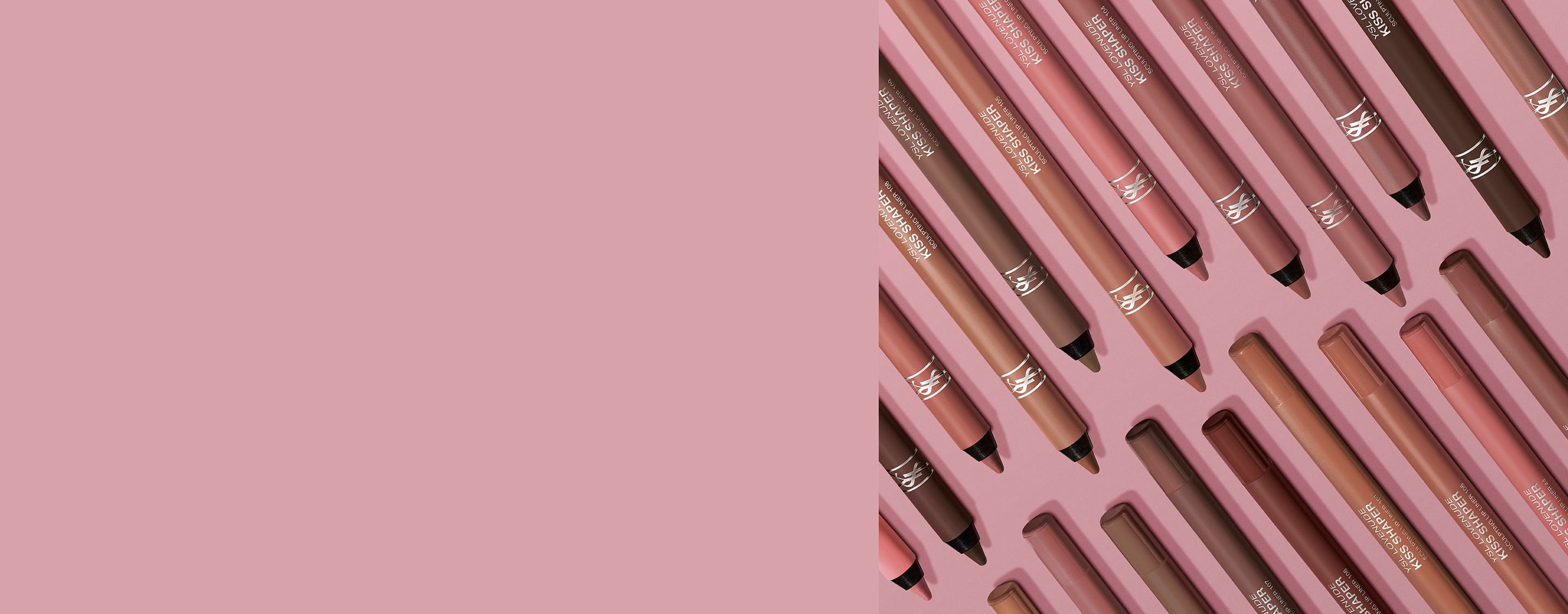 Gamma di matite labbra YSL Kiss Shaper in tonalità nude e marroni su sfondo rosa.