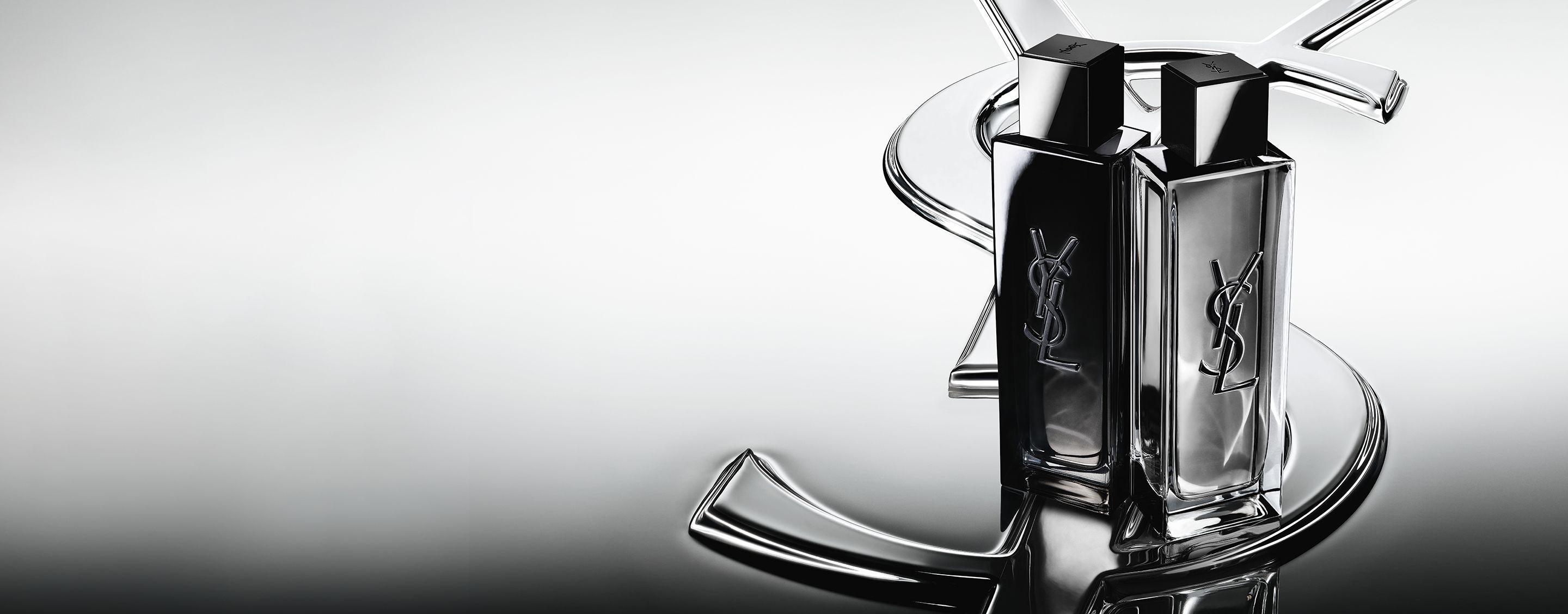 I flaconi di MYSLF Eau de Parfum e MYSLF Eau de Toilette Intense, affiancati su un grande logo Cassandre YSL con effetto specchiato.