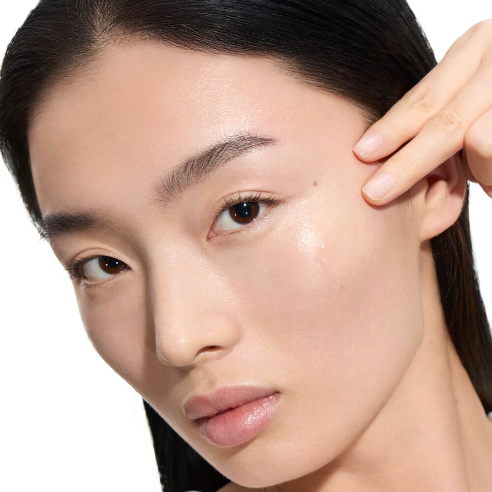 Wen, modella YSL Beauty, con pelle chiara, mentre applica una goccia di Pure Shots Youth Reload Serum sulla guancia.