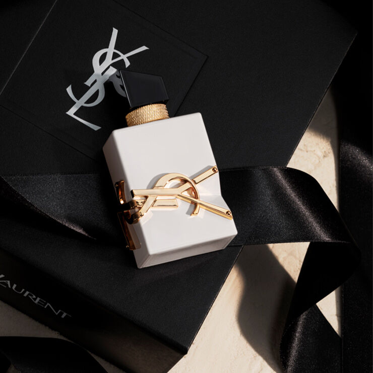Un elegante flacone bianco opaco di Libre appoggiato su una confezione regalo YSL nera con un nastro di seta.