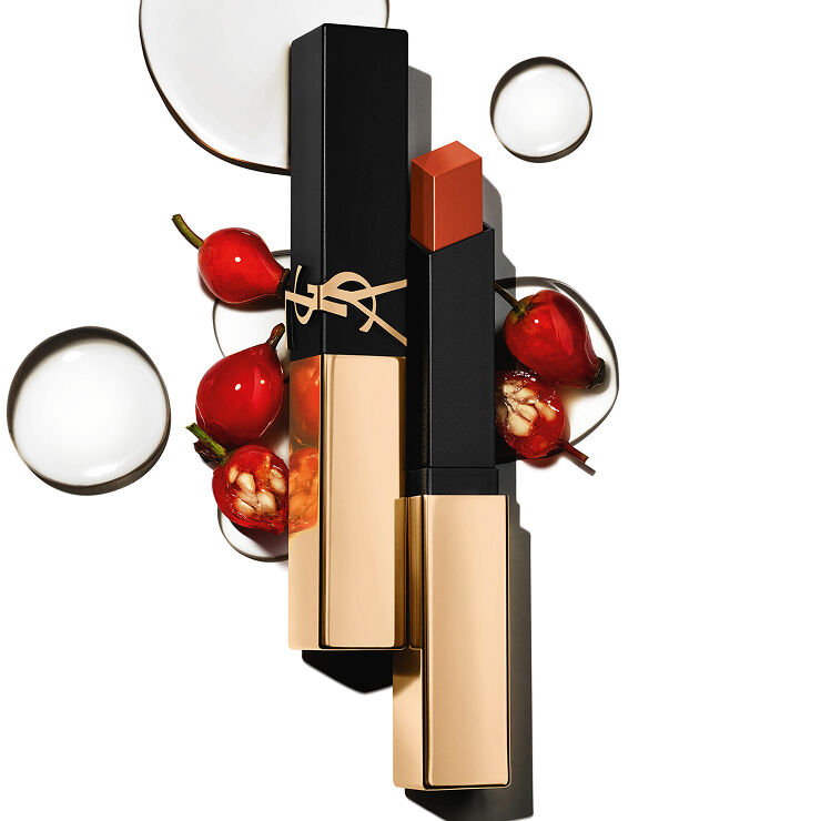 Rossetto quadrato YSL con cappuccio dorato tra bacche rosse e gocce trasparenti su fondo bianco.