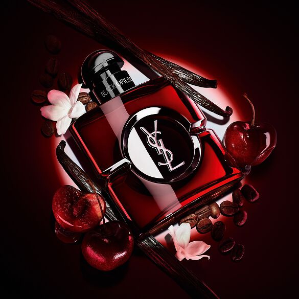Flacone Black Opium Over Red in lacca rosso intenso, circondato da ciliegie rosse fresche e chicchi di caffè tostato.