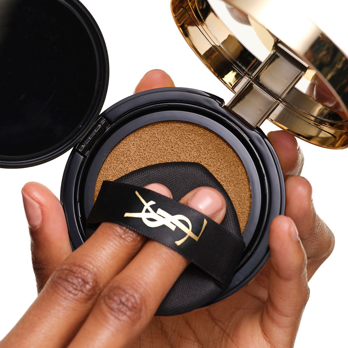 Carica il YSL SKIN AFFAIR SOFT GLOW CUSHION. Dita sotto il nastro nero con logo che premono il puff da trucco.