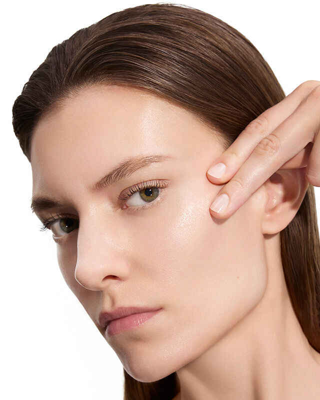Marije, modella di YSL Beauty, con pelle chiara, si sfiora delicatamente la guancia, mostrando una pelle levigata dopo l'applicazione della lozione.