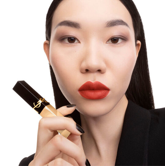 Mano che tiene un rossetto YSL quadrato nero e oro vicino al mento.