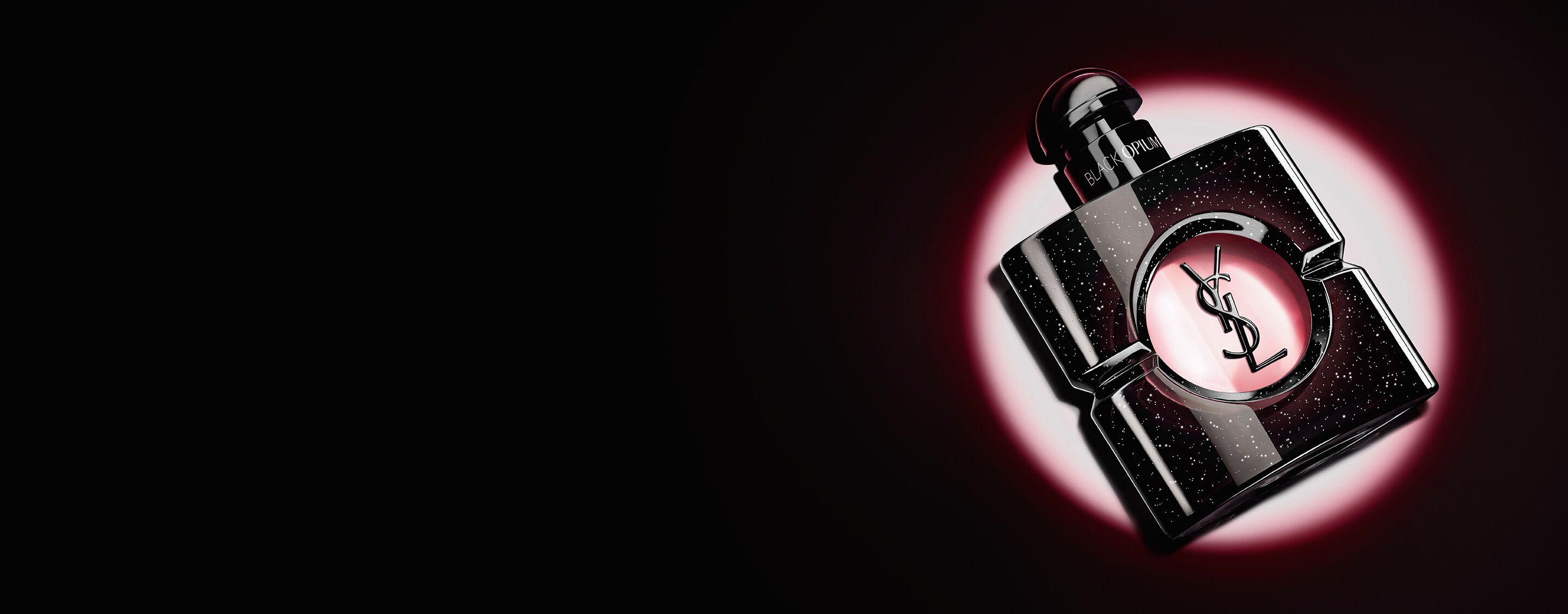 Flacone di Black Opium Eau de Parfum adagiato su un lato, su una superficie scura avvolta da un alone di luce rosa.