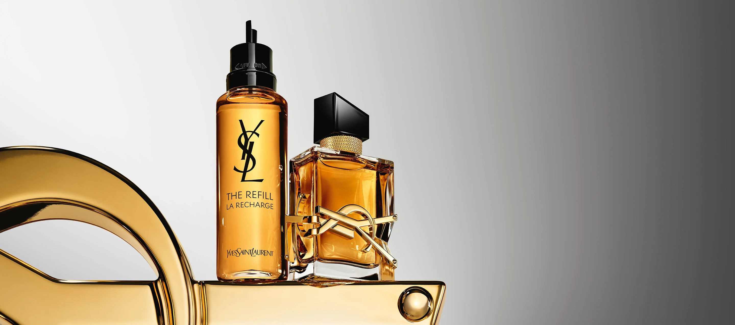 Due flaconi di profumo Yves Saint Laurent Libre, uno di ricarica, su un espositore dorato.
