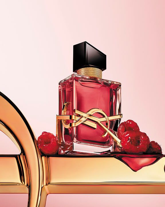 Primo piano di flacone di profumo YSL rosso con logo dorato su una superficie dorata con lamponi.